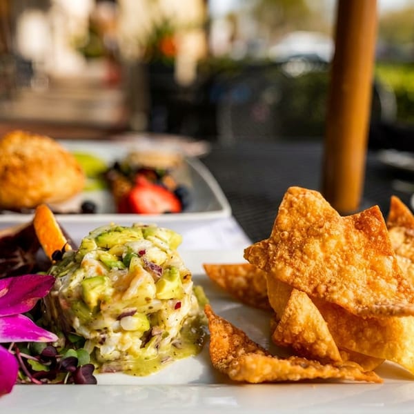 Appetizer plate with avocado salad, crispy wonton chips, and a purple orchid garnish on a white plate.